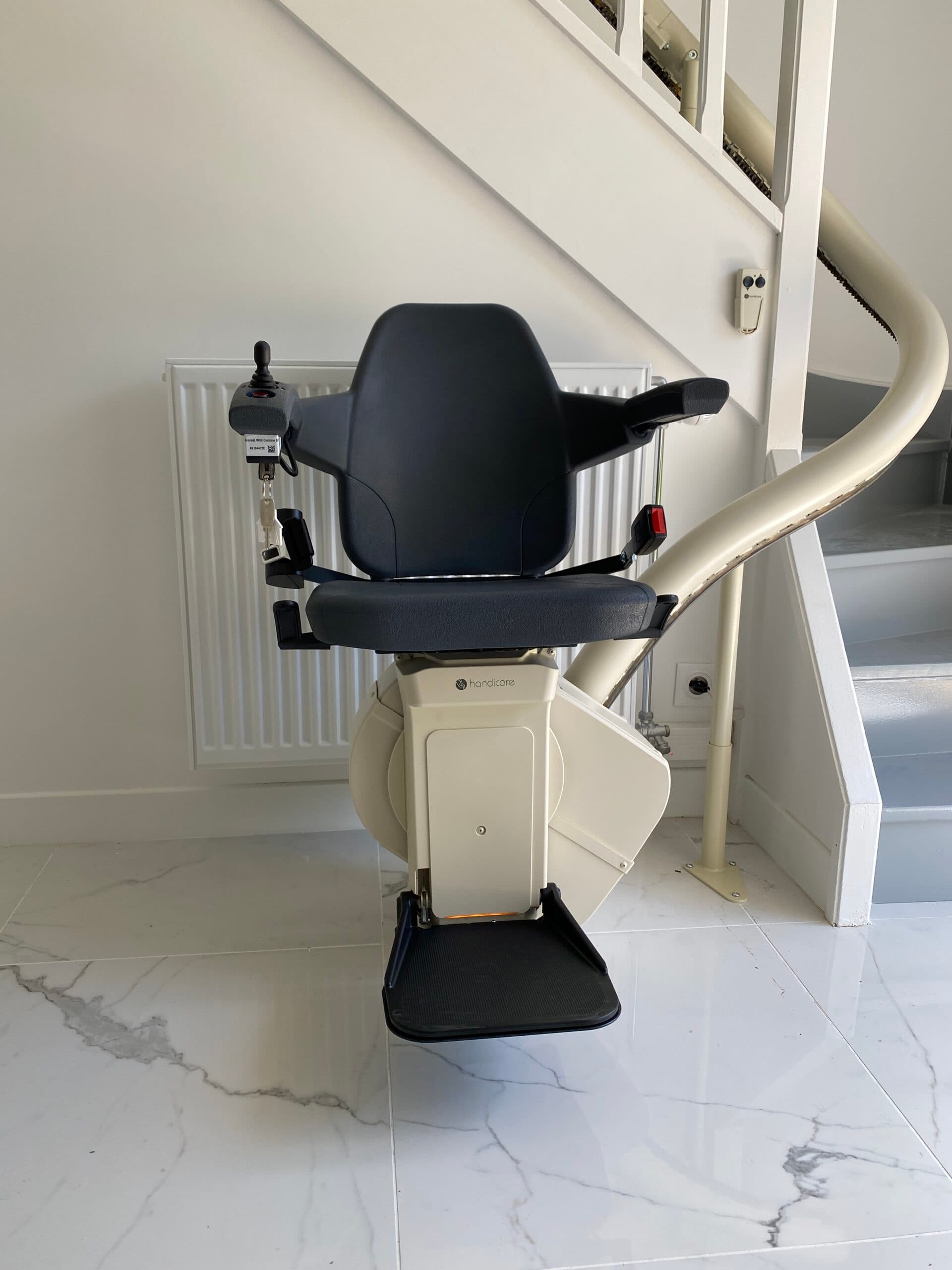 Monte-escalier avec siège noir installé au pied d'un escalier, vue de face
