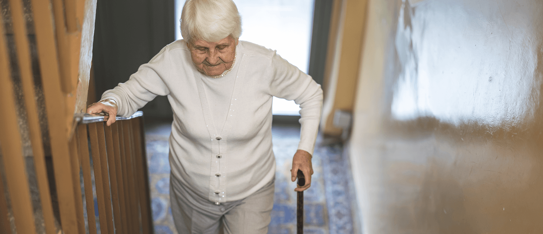 Une personne âgée descendant un escalier en s'appuyant sur la rampe et une canne