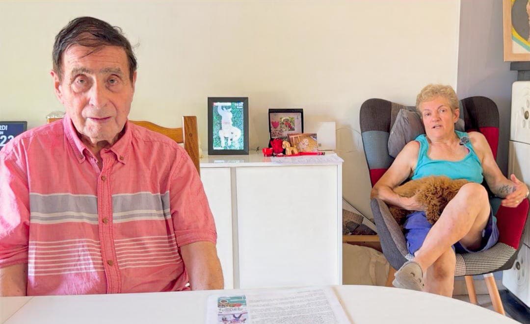 Un homme âgé assis à table et une aidante tenant un petit chien, lors d'un témoignage vidéo