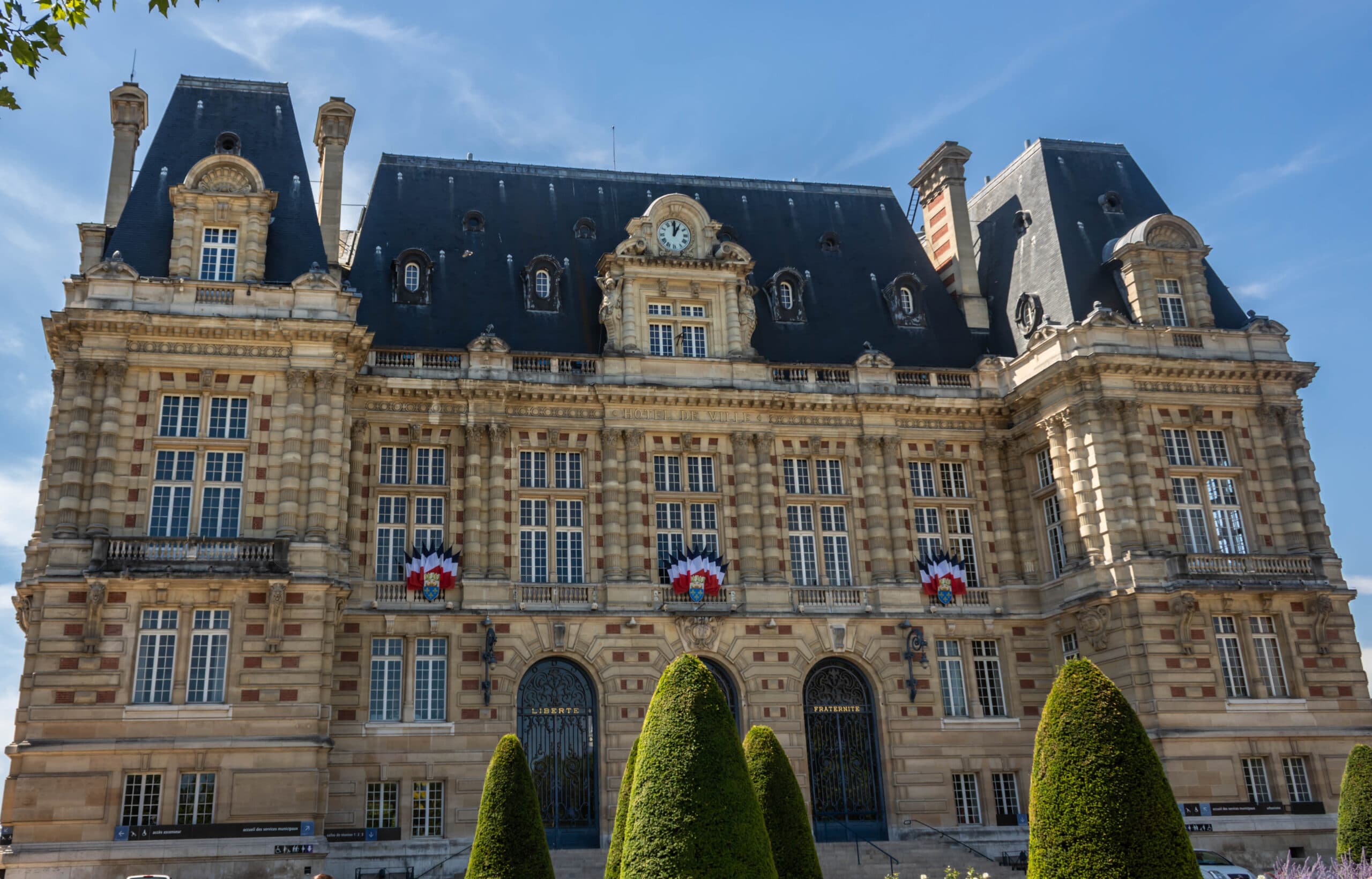 Façade d'un hôtel de ville de style classique, orné de drapeaux et cocardes tricolores