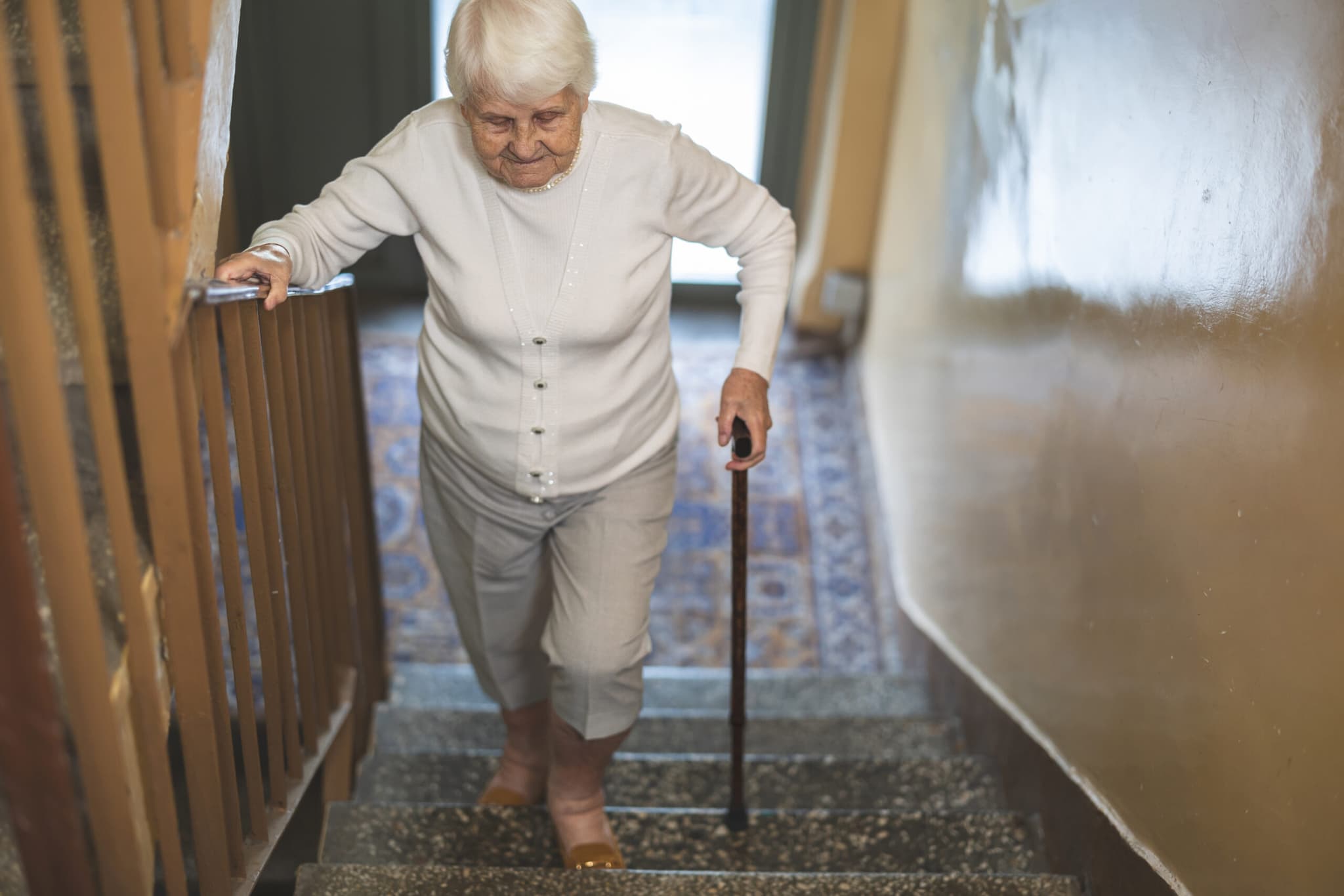 Une femme âgée descendant un escalier en s'appuyant sur la rampe et une canne