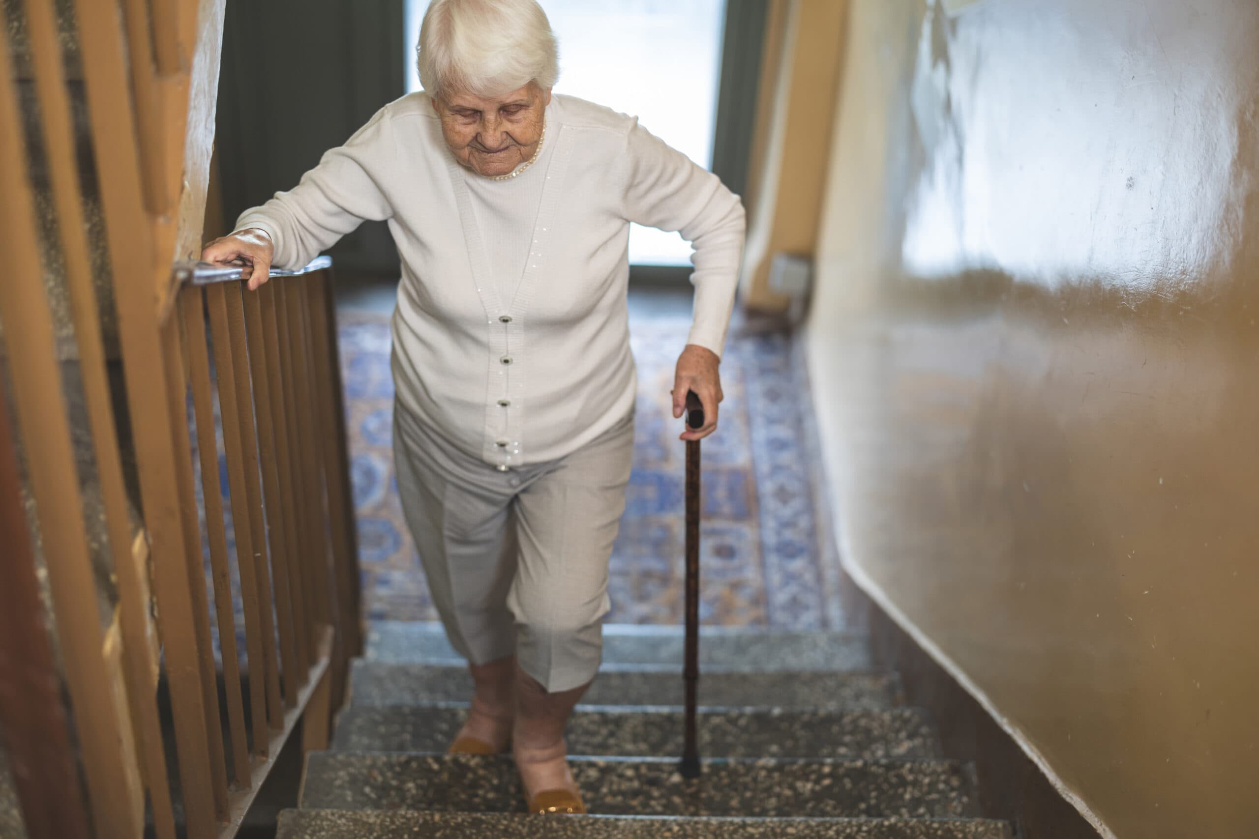 Une femme âgée descendant un escalier en s'appuyant sur la rampe et une canne