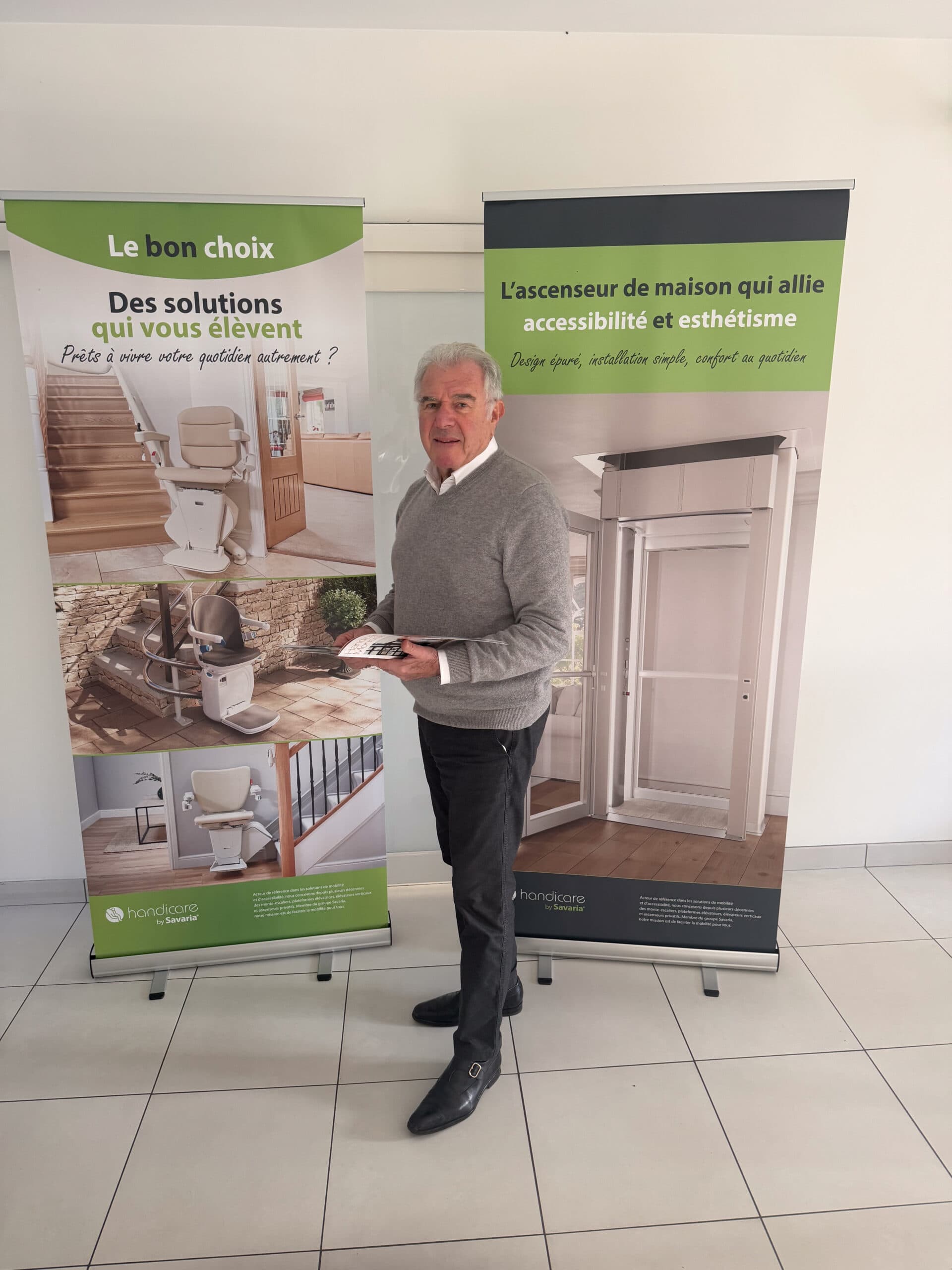 Un homme dans un showroom devant des banderoles présentant des monte-escaliers et un ascenseur de maison