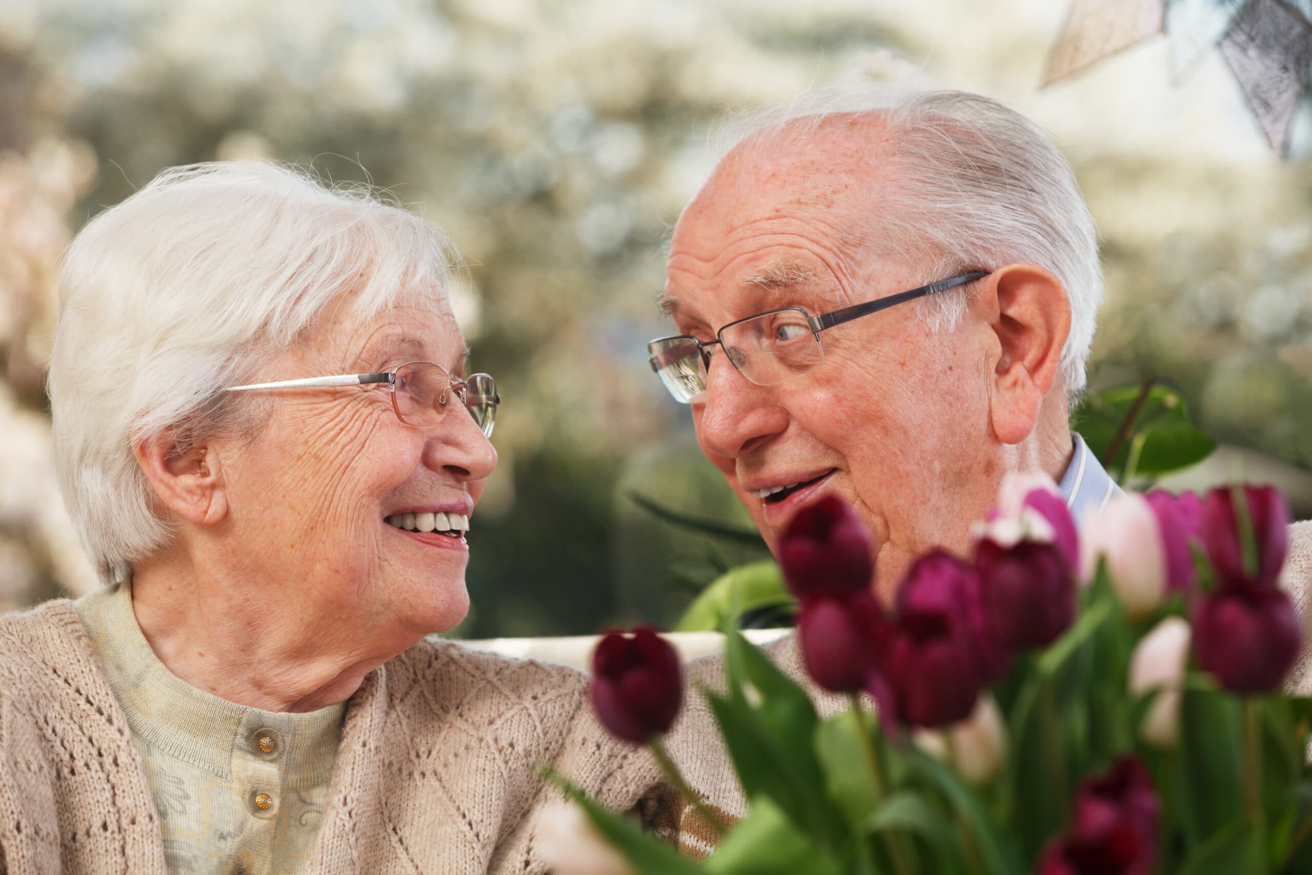 Un couple de personnes âgées souriant, entouré d'un bouquet de tulipes