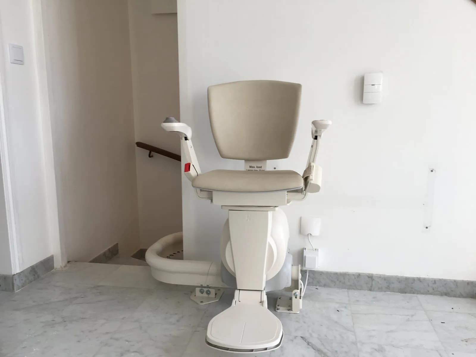 Monte-escalier électrique installé en haut d'un escalier intérieur, siège en position d'arrivée sur le palier
